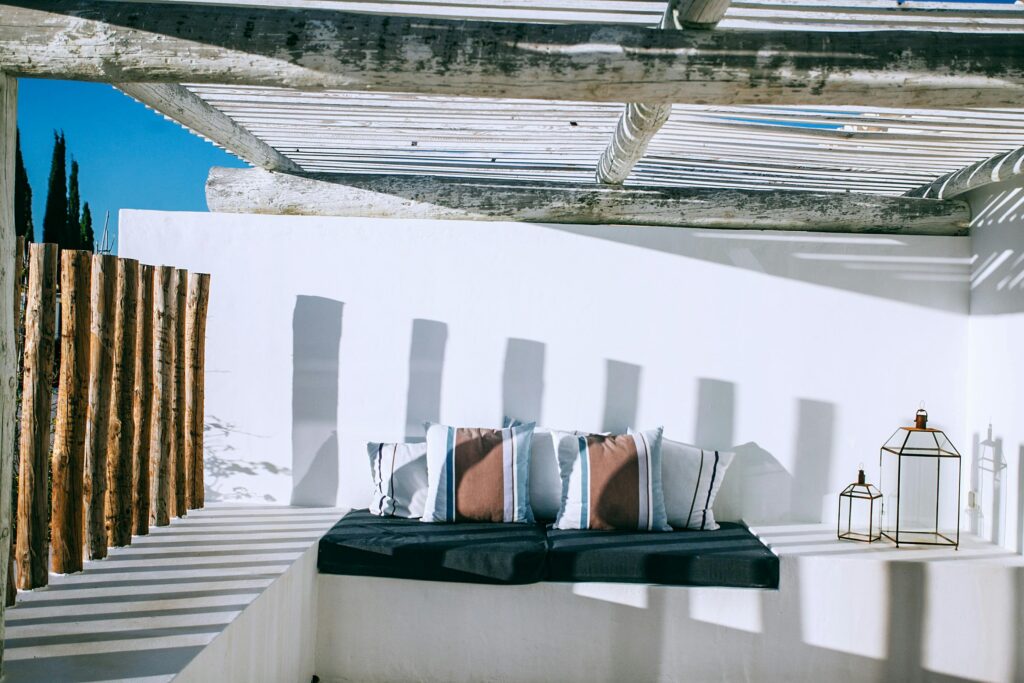 Relaxing outdoor terrace with stylish cushions under a wooden pergola in bright sunlight.